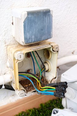 Yıpranmış ve hasarlı bir elektrik kablosu gösteriliyor, bileşenleri ortaya çıkıyor. Yakınlarda güvenlik ve güncelleme ihtiyacını vurgulayan yeni bir yedek kutu kuruldu.