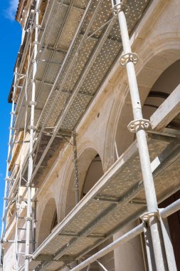 İşçiler tarihi bir binayı restore etmek için yapı iskelesini kullanırken, açık bir gökyüzü zeminine karşı inşaat çabalarını sergiliyor, takım çalışmasını ve korunma kararlılığını vurguluyor.