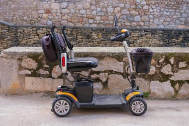 Valencia, İspanya - 22 Mart 2025: Engelli yaşlılar için elektrikli scooter sakin bir açık havada taştan bir duvara yaslandı