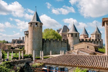 Carcassonne Kalesi etkileyici taş kulelerini ve ortaçağ mimarisini canlı bir gökyüzüne karşı sergiliyor. Ziyaretçiler, huzurlu ortamın ve keyifli atmosferin tadını çıkarırken antik kaleye hayran kalıyorlar..