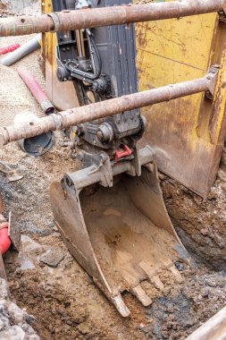 Ağır makineler bir inşaat alanında su boru hatlarını tamir etmekle meşgul. Kazıcının kovası yeraltı tesislerinin korunmasında gösterilen çabayı gözler önüne seriyor..