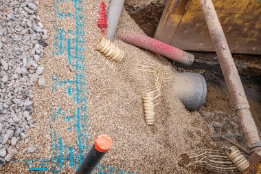 İşçiler su boru hatlarını tamir etmek için özel makineler kullanıyorlar. İnşaat sahasında çakıl ve borular görülebiliyor ve kentsel altyapı bakımı ve takım çalışması devam ediyor.