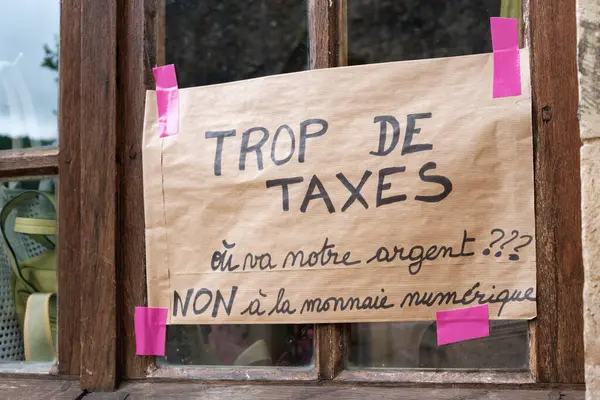 Yüksek vergilerin sorgulanması ve dijital para biriminden hoşnutsuzluğun dile getirilmesi, toplumsal duyguları ve yerel hüsranları yansıtan el yapımı bir protesto tabelası kırsal bir pencereye yerleştiriliyor..