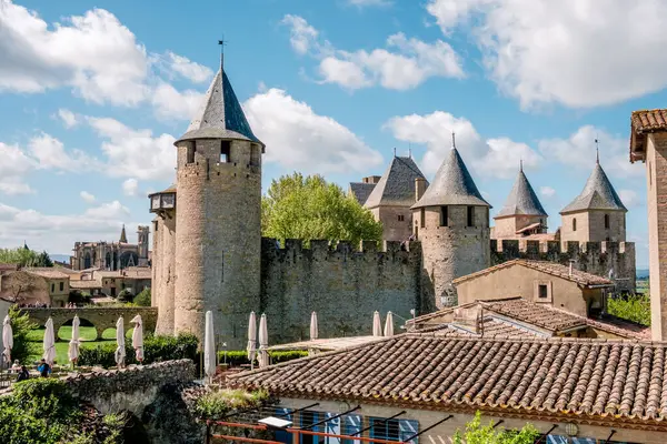 Carcassonne Kalesi etkileyici taş kulelerini ve ortaçağ mimarisini canlı bir gökyüzüne karşı sergiliyor. Ziyaretçiler, huzurlu ortamın ve keyifli atmosferin tadını çıkarırken antik kaleye hayran kalıyorlar..