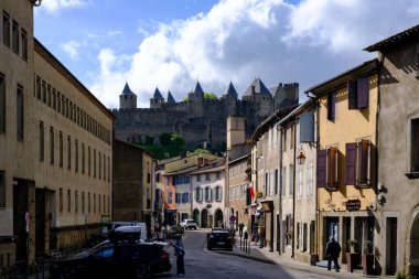 Toulouse, Fransa - 21 Nisan 2025: Carcassonne, Fransa 'da ortaçağ kale zeminine sahip tarihi sokak manzarası canlı mimari ve bulutlarla dolu gökyüzü