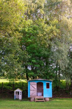 Parlak mavi bahçe kulübesi, canlı yeşillikler ve ağaçlarla çevrili tuhaf bir tavuk kümesinin yanında duruyor. Rahatlamak için mükemmel, sakin bir açık hava yaratıyor..