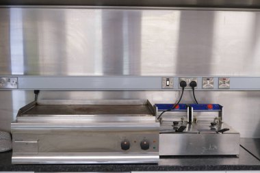 Paslanmaz çelik ızgara ve kızartma makinesi İngiltere 'de endüstriyel bir mutfakta parlak bir duvara dayalı olarak profesyonel şefler için verimli bir çalışma alanı sunuyor..