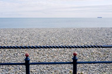 İrlanda 'daki sakin sahili keşfedin, yumuşak, bulutlu bir gökyüzünün altında yumuşak, yuvarlak çakıl taşlarının sakin sularla buluştuğu yeri. Dekoratif parmaklıklar sükunet ortamına biraz zarafet katar..