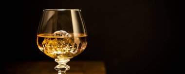 Glass of scotch whiskey and ice on old wooden table over black background. Banner with copy space
