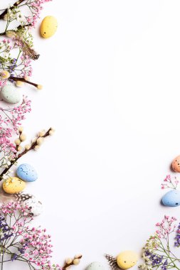 Border with Easter composition with spring flowers and colorful quail eggs over white background. Springtime and Easter holiday concept with copy space. Top view