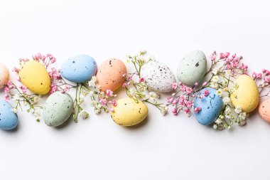 Easter composition of colorful quail eggs and spring flowers over white background. Springtime holidays concept with copy space. Top view