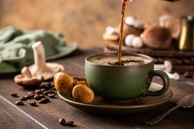 Trendy superfood mushroom coffee is pouring in green cup on wooden background. Healthy concept with copy space, selective focus.