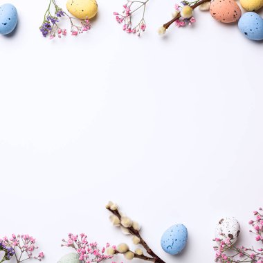 Border with Easter composition with spring flowers and colorful quail eggs over white background. Springtime and Easter holiday concept with copy space. Top view