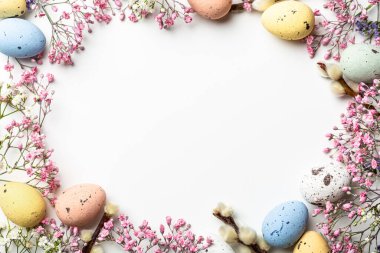 Overhead shot of Easter composition with spring flowers and colorful quail eggs over white background. Springtime and Easter holiday concept with copy space. Top view