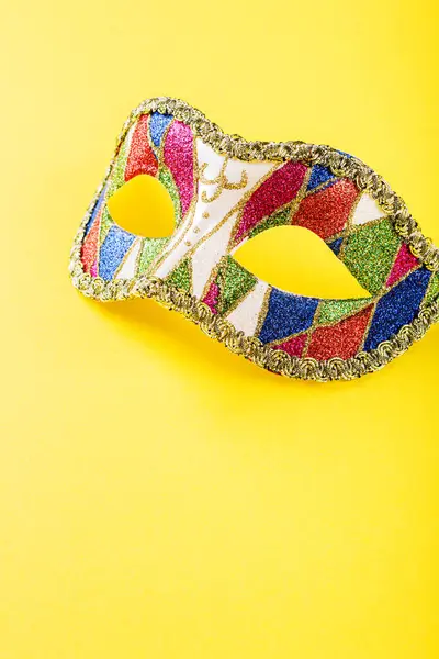 Vibrant image of a colorful masquerade mask adorned with intricate designs, placed against a bright yellow background. The mask is decorated with glittering patterns. Copy space.