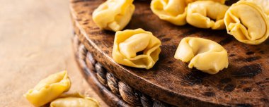 Taze pişmemiş İtalyan yemeği tortellini makarnasıyla sade ahşap bir panoda, sıcak desenli bir arka planda..