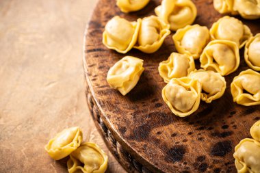 Köy tahtasının üzerinde pişmemiş tortellini makarna, fotokopi alanı olan sıcak desenli bir arka plan üzerine kurulmuş. Sağlıklı İtalyan yemeği konsepti, yüksek açı manzarası