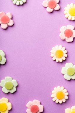 Mor bir zemin üzerine yerleştirilmiş çeşitli pastel çiçek şekilli jelibon şekerler, merkezinde boş bir boşluk olan oyuncu ve tatlı bir kompozisyon oluşturur.