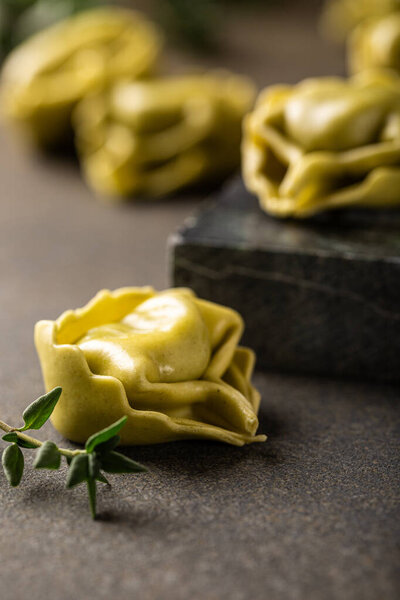 Fresh uncooked tortellini pasta with ricotta and spinach on a dark green textured board, garnished with fresh herbs for a rustic presentation. Healthy food concept
