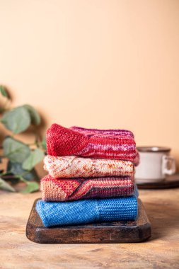 Sıcacık, davetkar bir atmosfer için sıcak bir kahve fincanı ve yeşillik içeren rahat bir arka planı olan rustik ahşap bir tahtanın üzerinde düzgünce dizilmiş el örgüsü yün çoraplar yığını. Boşluğu kopyala
