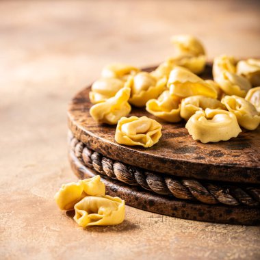 Köy tahtasının üzerinde pişmemiş tortellini makarna, fotokopi alanı olan sıcak desenli bir arka plan üzerine kurulmuş. Sağlıklı İtalyan yemeği konsepti