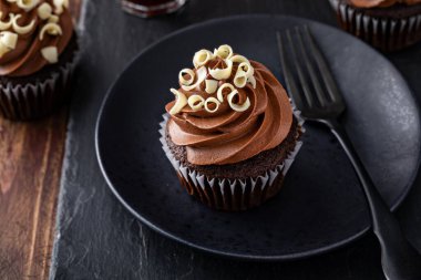 Chocolate cupcakes with dark chocolate ganashe frosting on dark background clipart