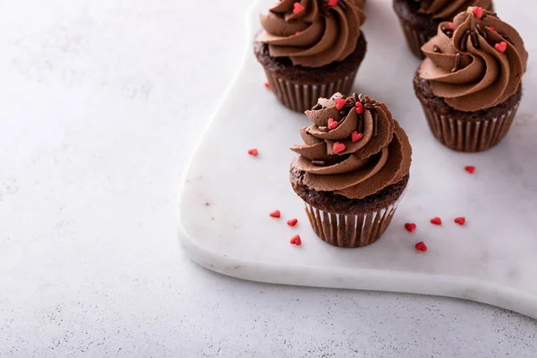 Dark chocolate mini cupcakes with chocolate ganache frosting and heart sprinkles for Valentines day, copy space