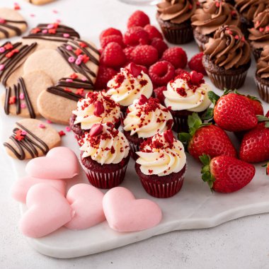 Valentines day charcuterie board or dessert snack board with cupcakes, cookies and strawberries