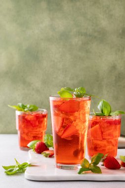 Strawberry basil cocktail or mocktail, cold refreshing summer drink on green background with copy space