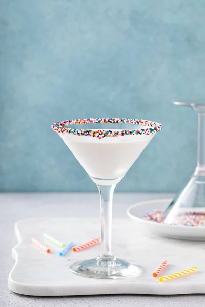 Birthday cake martini with sprinkles on the glass rim and birthday candles