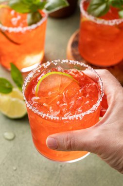Strawberry basil margarita with lime, hand holding a glass, refreshing summer cocktail