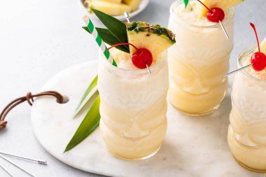 Tropical pina colada cocktail or mocktail in a tiki glass with pineapple and cherry