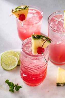 Singapore sling cocktail in variety of glasses garnished with pineapple and cherry