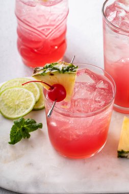 Singapore sling cocktail in variety of glasses garnished with pineapple and cherry