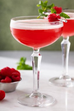 Raspberry martini cocktail with vodka, pineapple juice and raspberry liqueur garnished with mint