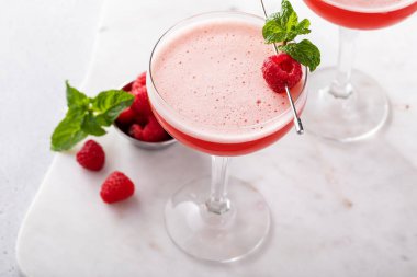 Raspberry martini cocktail with vodka, pineapple juice and raspberry liqueur garnished with mint