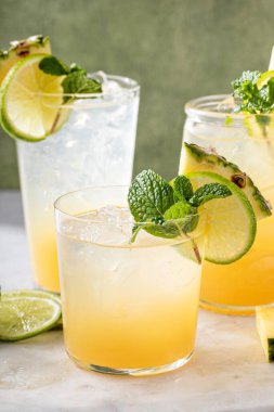 Mai tai cocktail in different glasses garnished with pineapple, lime and mint