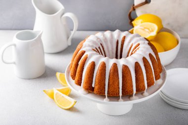 Lemon bundt cake drizzled with powdered sugar glaze on a cake stand