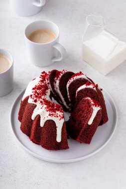 Red velvet bundt cake with cream cheese frosting and cake crumbs on top sliced on a plate