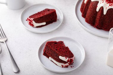Red velvet bundt cake with cream cheese frosting and cake crumbs on top slices on a plate