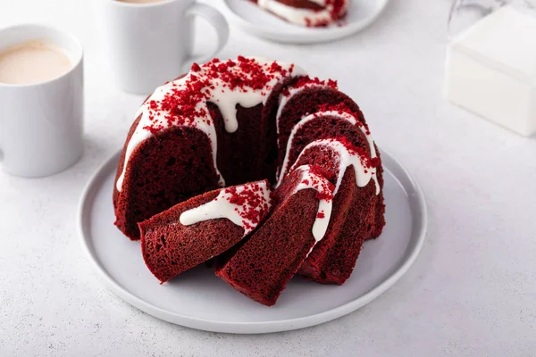 Red velvet bundt cake with cream cheese frosting and cake crumbs on top sliced on a plate