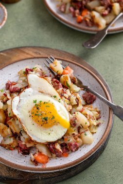 Corned beef hash with potatoes, cabbage and carrot on a plate topped with a fried egg