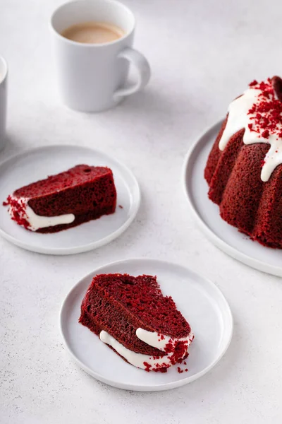 Red velvet bundt cake with cream cheese frosting and cake crumbs on top slices on a plate