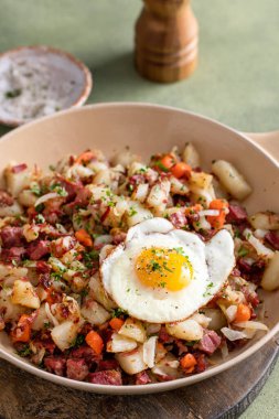 Corned beef hash with potatoes, cabbage and carrot in a cast iron pan topped with a fried egg