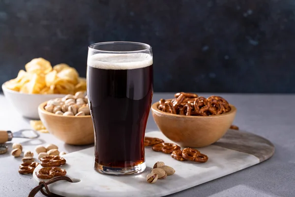 Dark stout beer in a tall glass, beer and snacks on the table