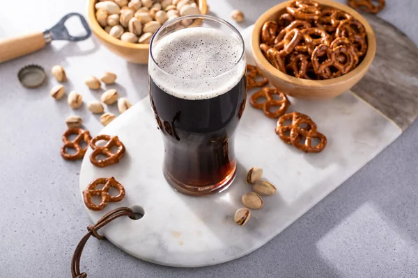 Dark stout beer in a tall glass, beer and snacks on the table