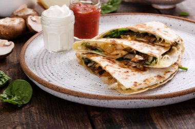 Salsa ve ekşi kremayla servis edilen bir tabakta dilimlenmiş biftek ve mantarlı quesadilla.