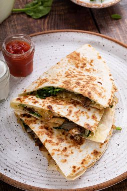 Salsa ve ekşi kremayla servis edilen bir tabakta dilimlenmiş biftek ve mantarlı quesadilla.