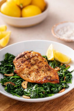 Kızarmış tavuk sotelenmiş ıspanak ve limon, sağlıklı akşam yemeği fikri.