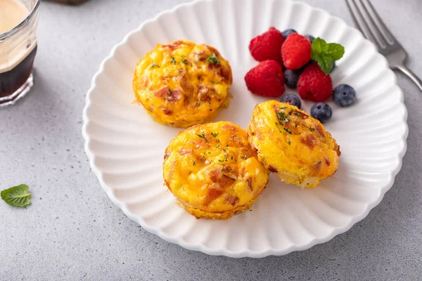 Breakfast egg muffins or egg bites with potato, bacon and cheddar served with fresh berries